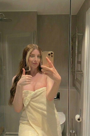 Curvy woman with long hair in towel in bathroom selfie.