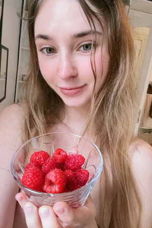 Woman with wavy hair holding raspberry bowl, topless in bathroom.