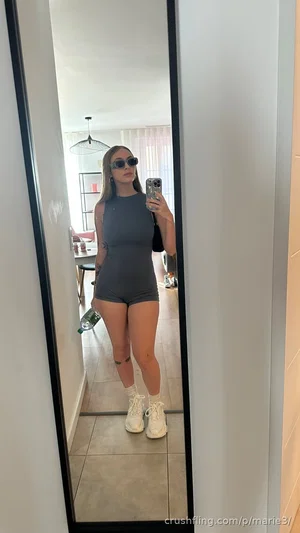 Woman in gray bodysuit and white sneakers takes mirror selfie in indoor setting.