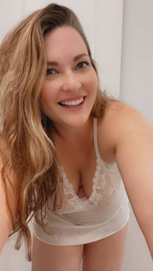Curvy blonde woman smiling in white lace top indoors.