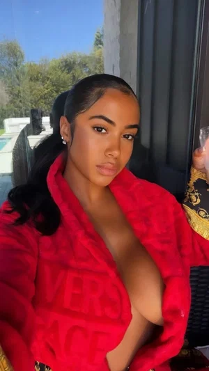 Woman in red robe with deep neckline, holding drink, outdoors near pool.