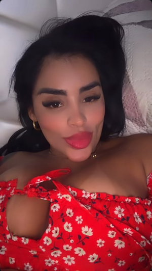 Woman with dark hair in red floral off-shoulder top lying on bed.