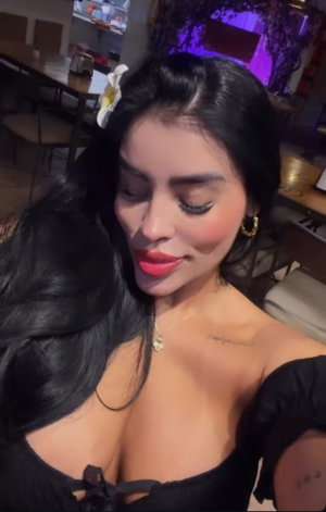 Woman with long black hair and red lips in black off-shoulder top, indoors.