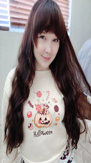 Woman with long brown bangs in Halloween sweatshirt indoors.