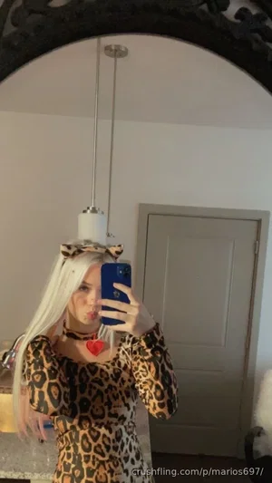 Woman with long blonde hair in leopard print dress and choker, taking mirror selfie indoors.