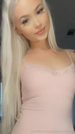 Woman with long platinum hair in a light pink lace-trimmed camisole, indoors.
