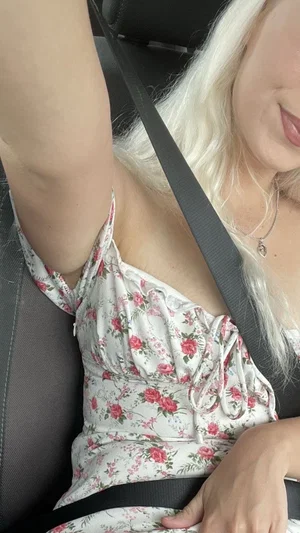 Blonde woman in floral top sitting in car, wearing seatbelt.
