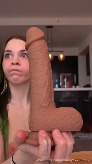 Woman with green hair holding a large brown object indoors, bare shoulders visible.