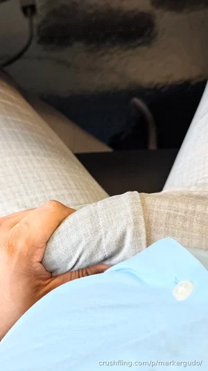Person in light blue shirt and beige pants, sitting indoors with hand on knee.