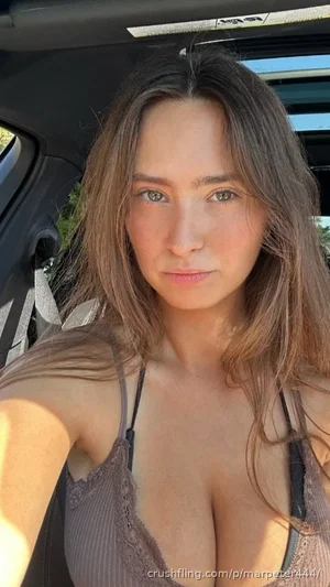 Woman with long brown hair in a lace bra top, taking selfie inside a car.