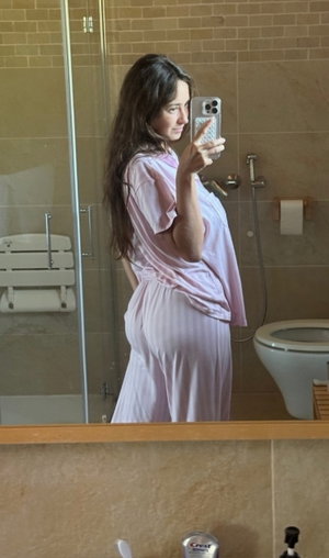 Woman in pink robe taking mirror selfie in bathroom.