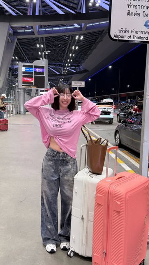 Woman in pink shirt and jeans posing at airport with luggage.