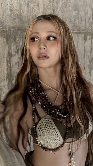 Asian woman with long blonde hair in crocheted top and necklaces.