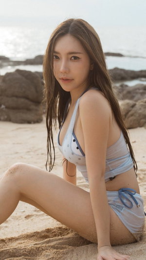 Woman in bikini sitting on beach sand.