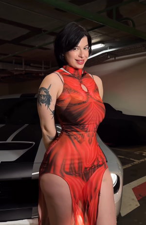 Woman in red patterned dress with high slit, standing in garage next to car.