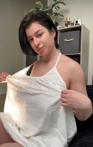 Woman with short dark hair in white top, sitting indoors, holding fabric.