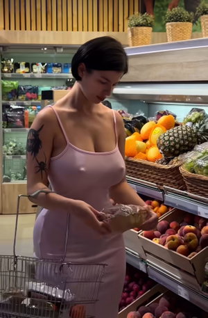 Woman in pink dress with tattoos shopping for fruit in grocery store.