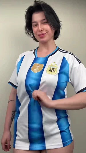 Woman with short dark hair wearing Argentina soccer jersey, standing indoors.