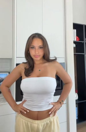 Woman in white strapless top and light pants posing in kitchen.