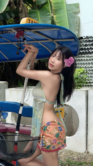 Woman with dark hair in sheer top and shorts outdoors.