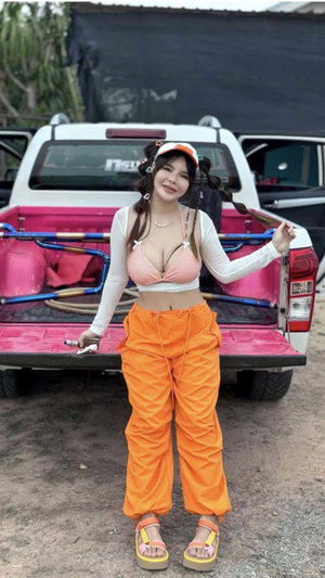 Woman in pink top and orange pants by pink truck.