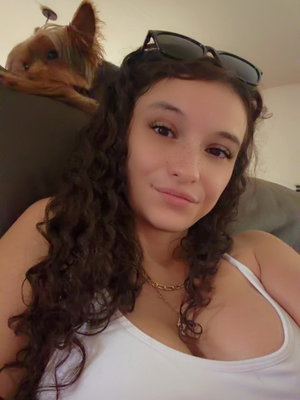 Woman with long curly hair in white tank top indoors.