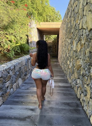 Woman with long dark hair in colorful crochet shorts walking on stone path outdoors.