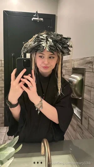 Woman in black outfit with leaf crown takes mirror selfie in bathroom.