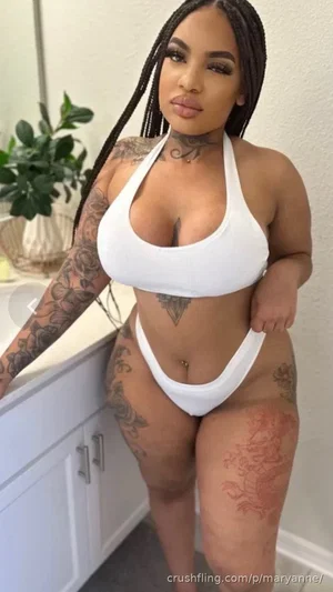 Woman with tattoos in white bikini posing in bathroom.