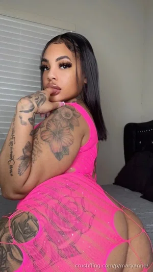 Woman with tattoos in pink mesh dress posing indoors.