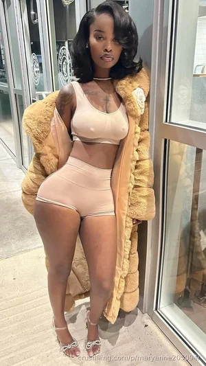 Woman in beige lingerie and fur coat posing outdoors near glass doors.