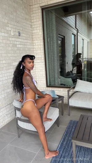 Woman with long curly hair in purple bikini posing on patio chair, outdoor setting.