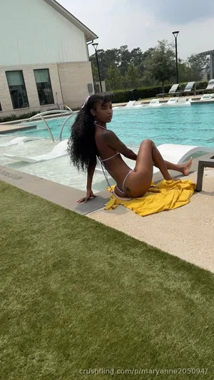 Woman in white bikini sits by poolside on yellow towel, long dark hair, outdoor setting.