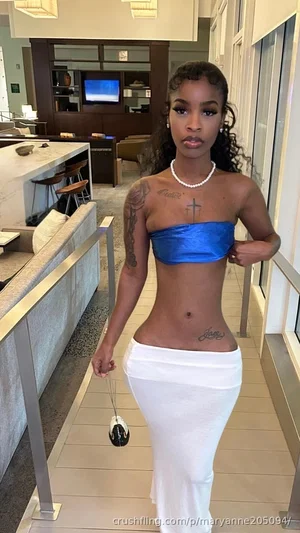 Woman with curly hair in blue strapless top and white skirt, standing in modern indoor space.