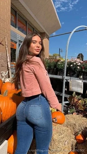 Woman in pink crop top and jeans posing with pumpkins outdoors.