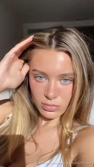 Woman with blonde hair and blue eyes wearing a white top, posing indoors.