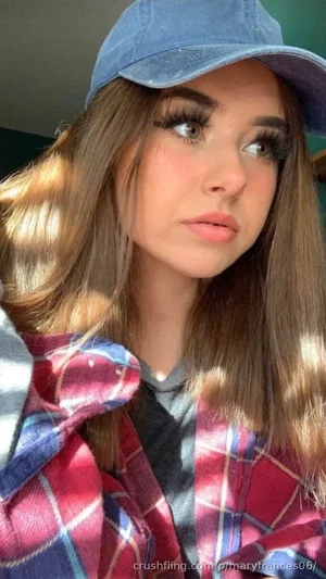 Woman with long brown hair wearing a denim cap and plaid shirt, looking up indoors.