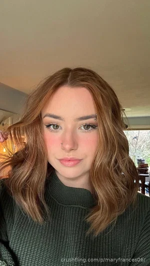 Woman with wavy brown hair, wearing a dark green turtleneck, indoors.