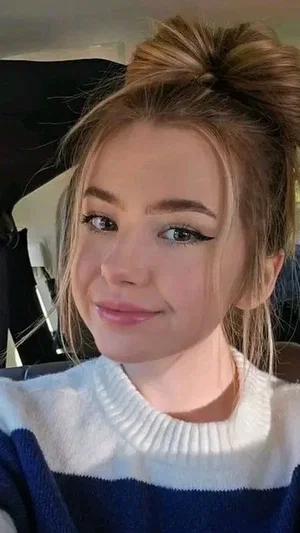 Woman with blonde hair in bun, wearing blue and white sweater, smiling in car.