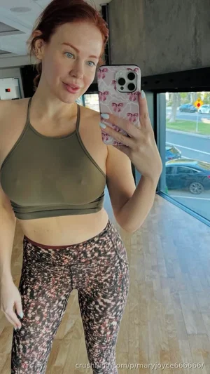 Woman in olive sports bra and patterned leggings takes mirror selfie indoors.