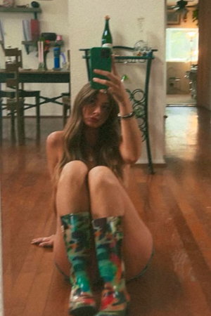 Woman with long hair taking a selfie indoors wearing colorful boots.