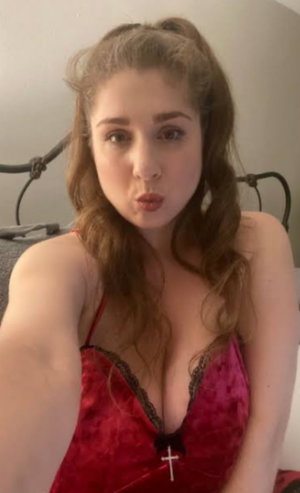 Woman in red lace lingerie with cross pendant, sitting indoors, hair in pigtails.