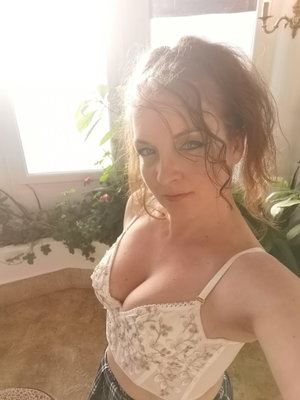 Woman with auburn hair in white lace top taking indoor selfie.