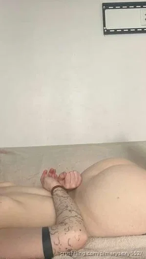 Person lying on bed, back to camera, showing bare buttocks and tattooed arm, indoor setting.