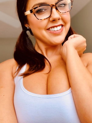 Woman with glasses and ponytail wearing light blue tank top indoors.