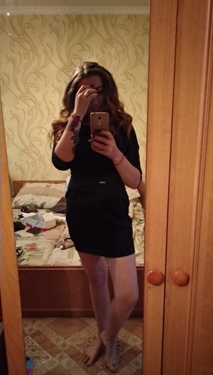 Brunette woman in short black dress, barefoot in bedroom.