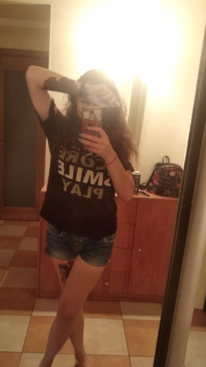 Woman in t-shirt and shorts taking mirror selfie indoors.