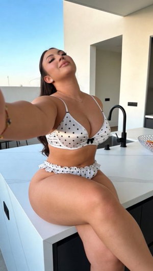 Woman in white polka dot bikini posing on kitchen counter, indoor setting.