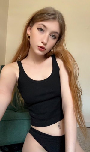 Woman with long hair in black crop top and underwear, sitting indoors.