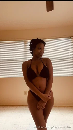 Woman in black lingerie posing indoors near window with blinds.